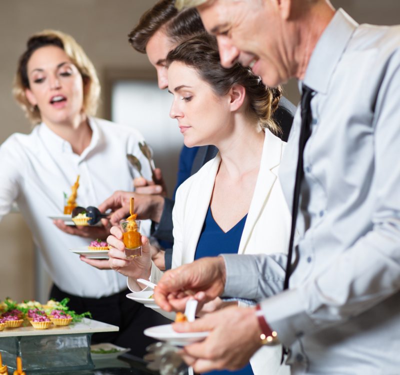 Group of five business people standing in buffet of restaurant and serving themselves with snacks. Catering concept