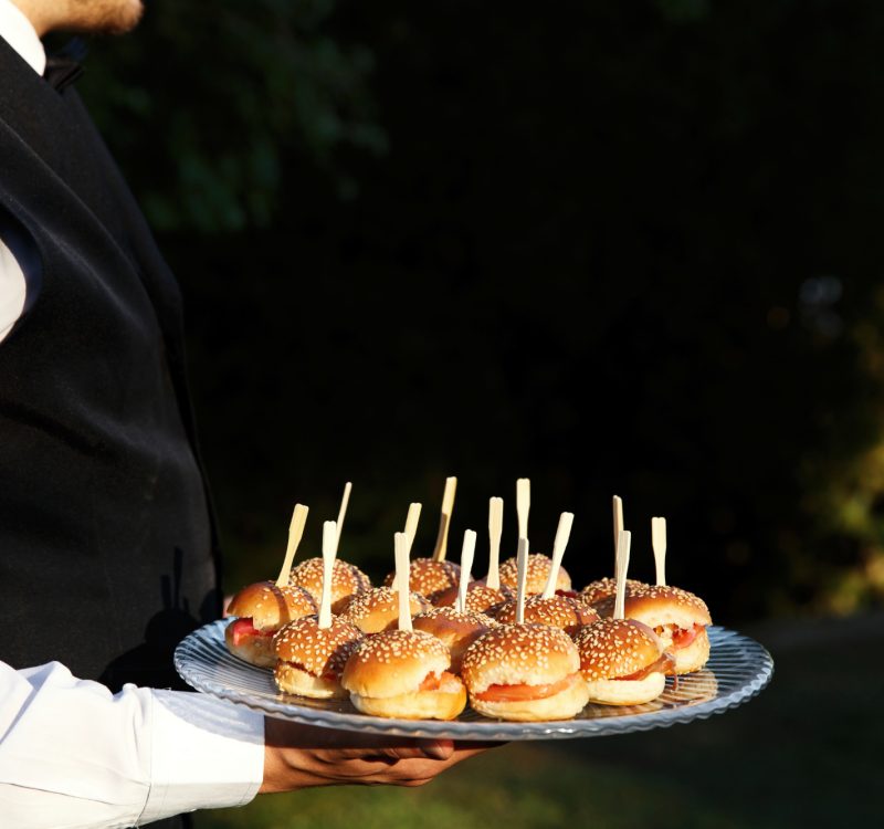 Tiny burgers served on a plate held by the waiter